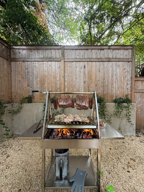 OctaGrills Argentina V-shaped parrilla grill, Santa Maria style, cooking lamb chops, sausage, and chicken over open fire at a Queens NY Astoria BBQ.