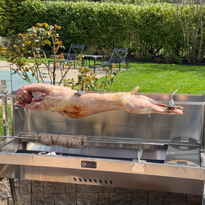 Outdoor setting with a large grill on a patio, featuring a whole lamb being roasted on a spit.  Seen here with our optional add on skewer kit spinning a kokoretsi on a souvla.