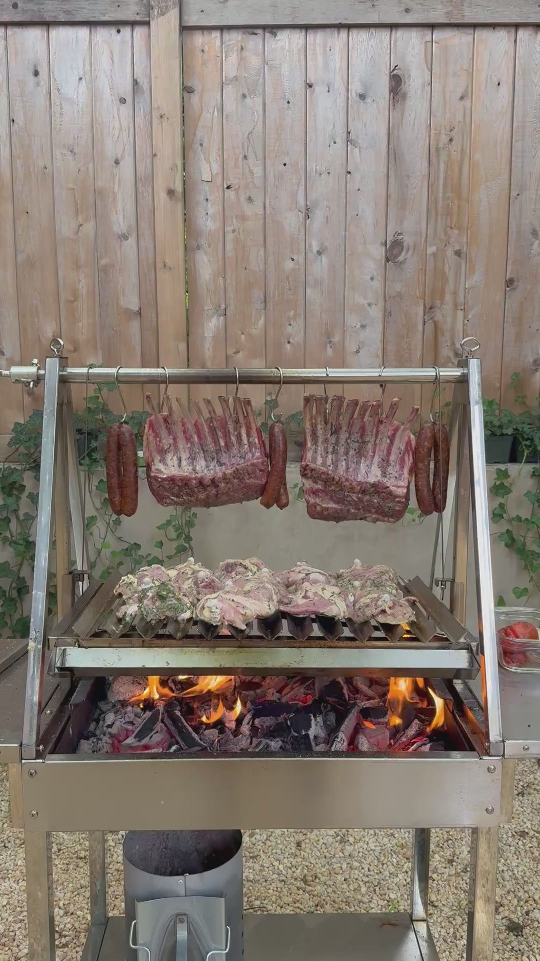 OctaGrills Argentina V-shaped video sizzling charcoal parrilla grill, Santa Maria style, cooking lamb chops, sausage, and chicken over open fire at a Queens NY Astoria BBQ.